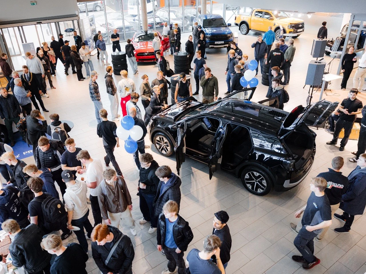 Oversiktsbilde av bilhallen til Auto 8-8 sett ovenfra, Ford Explorer i midten omgitt av ca 30 mennesker, ballonger og varebiler i bakgrunnen