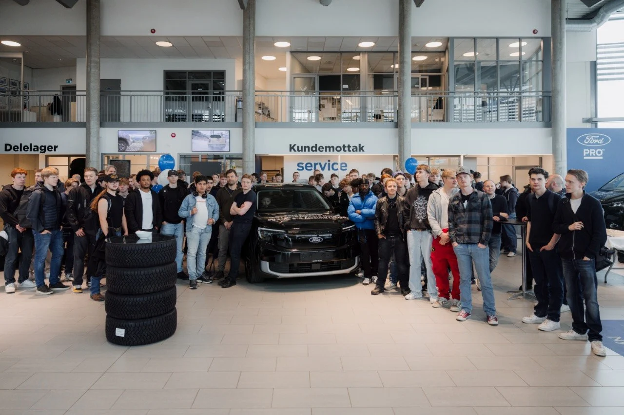 Stor flokk lærlinger og elever oppstilt foran Ford Explorer ved Kundemottak service-vegg, dekkstabel i forgrunnen