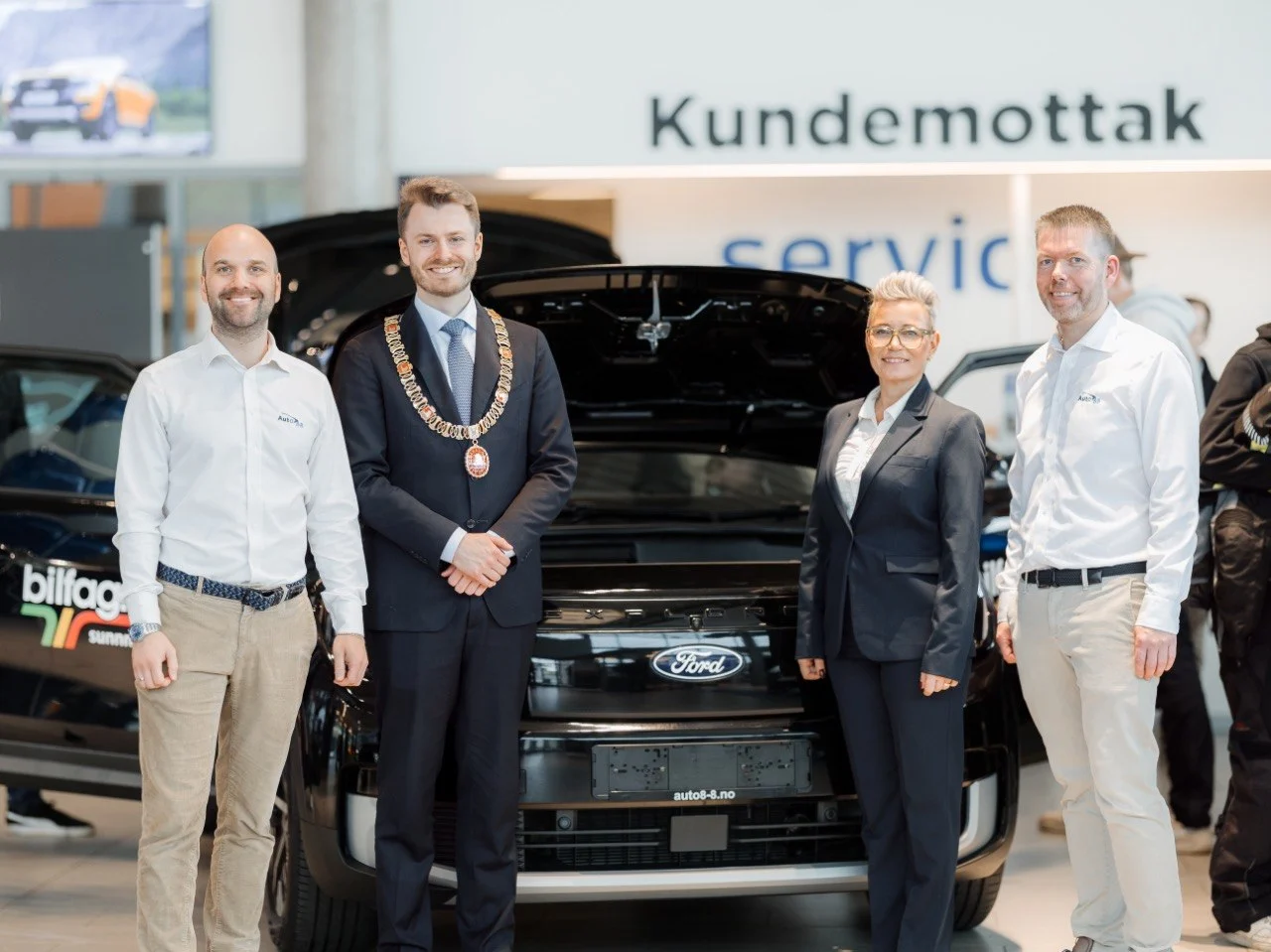 Fire personer i posert linje foran Ford Explorer ved Kundemottak service-skiltet: Roar Måseide, ordfører Håkon Lykkebø Strand med ordførerkjede, kvinne i mørk dress, og kollega