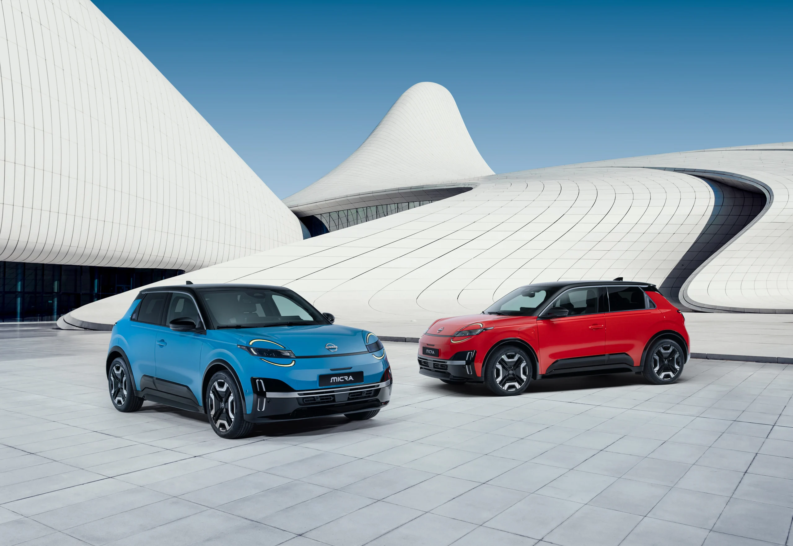To Nissan MICRA, én blå og én rød, foran en hvit bygning
