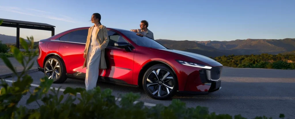 Mazda6e Homura Plus i Soul Red Crystal, sett fra siden i solnedgang med fjell i bakgrunnen