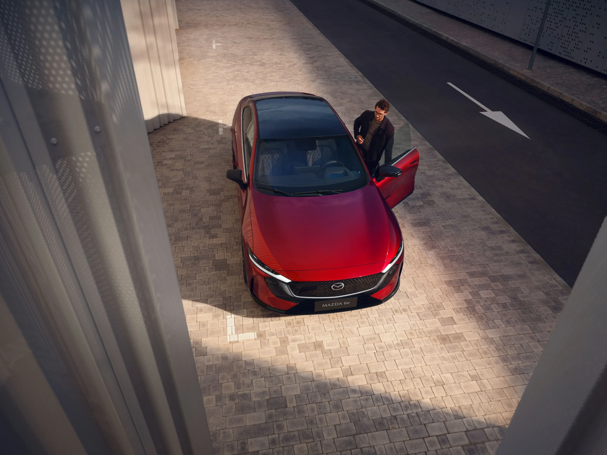 Mazda6e Homura Plus sett ovenfra i en smal passasje, med føreren på vei inn i bilen